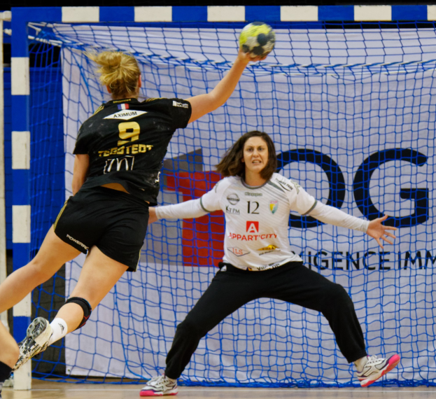 Zwei Frauen beim Handballspielen vor einem Tor, eine hält den Ball.