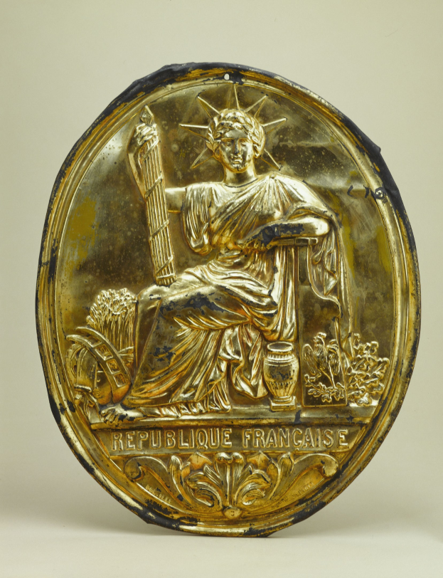 Goldenes rundes Schild mit einer Miniatur-Statue der Freiheitsstatue und eingraviertem Text auf einem weißen Hintergrund.