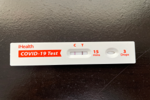 Ein weißer und roter Covid-19-Testthermometer mit Text und Zahlen darauf, auf einer schwarzen Oberfläche platziert.