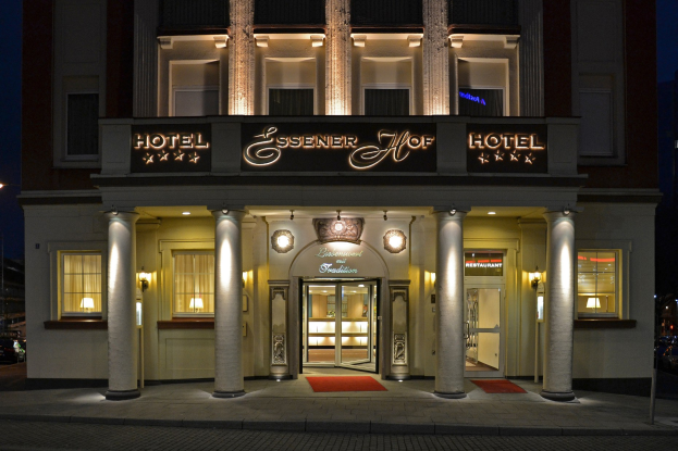 Das Essenerhof Hotel in Berlin, Deutschland, ein mehrstöckiges Gebäude mit Fenstern, Türen, Säulen und einem Namensschild, mit einer Straße und Fahrzeugen davor und einem klaren Himmel im Hintergrund.
