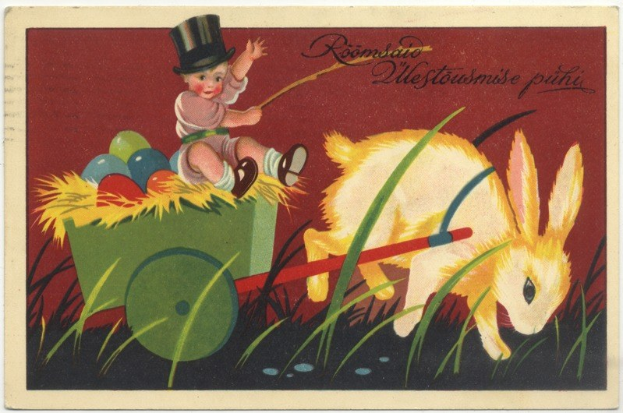 Alte Postkarte mit einem Baby in einem Zylinder, das einen mit bunten Ostereiern gefüllten Handkarren schiebt, begleitet von einem Kaninchen, mit handgeschriebener Textzeile zum glücklichen Osterfest.