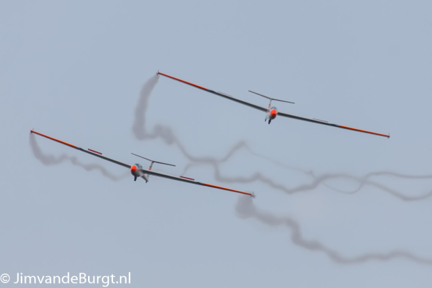 Zwei Segelflugzeuge mit Rauchspuren am Himmel, Text in der linken unteren Ecke.