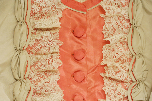 Nahaufnahme eines rosafarbenen und cremefarbenen Kleides mit weißer Spitze und vorderen Knöpfen.