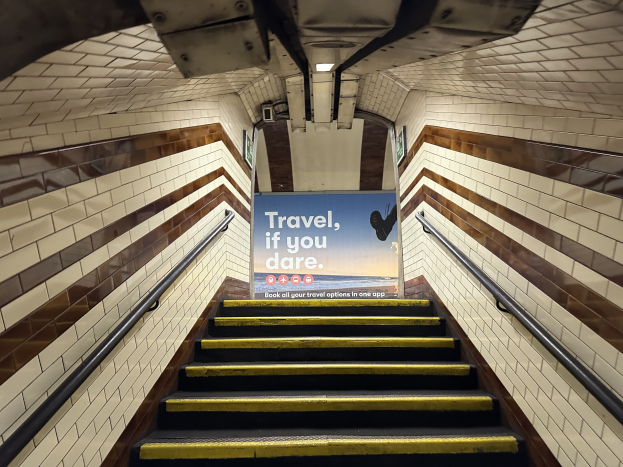 Eine Treppe in einer U-Bahn-Station mit einem Schild, das 'Reise, wenn du wagst' oben trägt, flankiert von Geländern und sichtbaren Stationswänden im Hintergrund.
