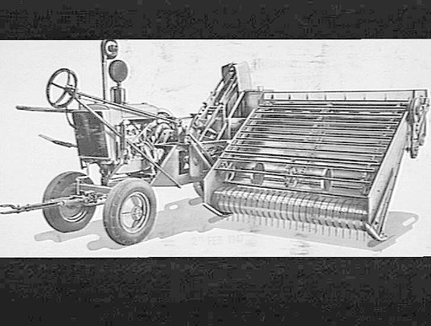 Schwarzes und weißes Foto eines Traktors mit einem angebauten Mähdrescher, mit einem großen Vorderrad und einem kleineren Hinterrad.