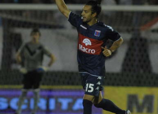 Ein Fußballspieler feiert auf dem Boden nach einem Tor, mit einer jubelnden Menge und einer Person im Hintergrund, alles mit einem unscharfen, energetischen Hintergrund.