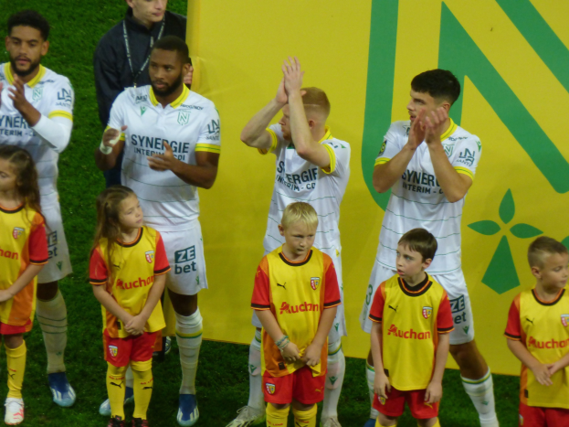 Eine Gruppe von Fußballspielern in Uniform klatscht auf einem Ligue 1-Feld in celebration, mit einem "Ligue 1" Schild im Hintergrund.