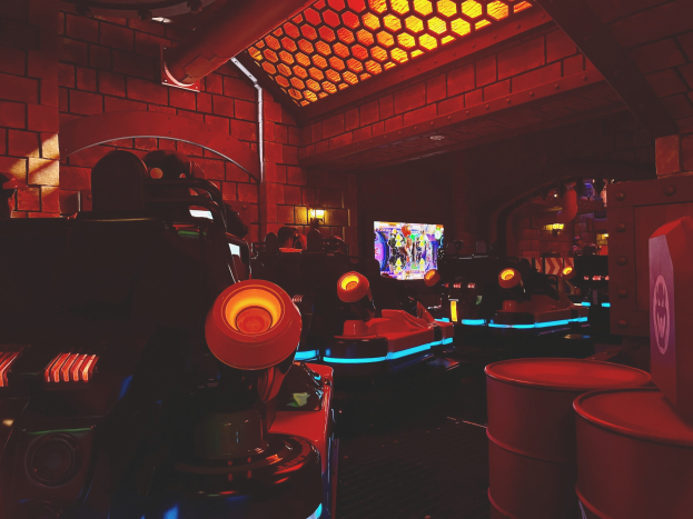 Ein hell erleuchteter Raum voller verschiedener Arcade-Videospielautomaten, Bildschirme und anderer Ausrüstung, der eine energiegeladene Atmosphäre schafft.