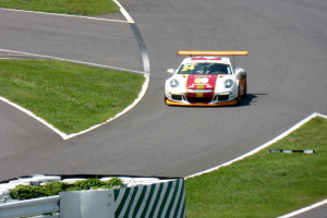 Ein Porsche 911 GT3 RSR auf der Nürburgring 24 Stunden Rennstrecke, umgeben von grünem Gras und einem Geländer, mit seinen leuchtenden Farben und seiner schlanken Form zu sehen.