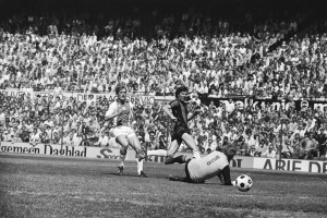 Schwarzes Foto von Fußballspielern im Einsatz auf einem Feld mit Zuschauern im Hintergrund und einer Bundesliga 1978-79-Wimpel.