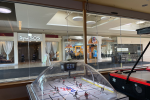 Eislaufbahn in einem Einkaufszentrum, umgeben von Glaswänden, mit einem Air-Hockey-Tisch auf der rechten Seite.