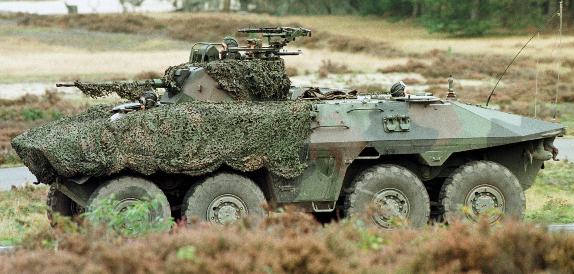 Militärpersonenwagen mit montierter großer Kanone auf einer Straße neben einem Wald.