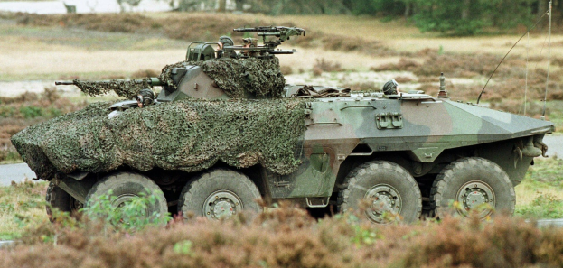 Militärpersonenwagen mit montierter großer Kanone auf einer Straße neben einem Wald.