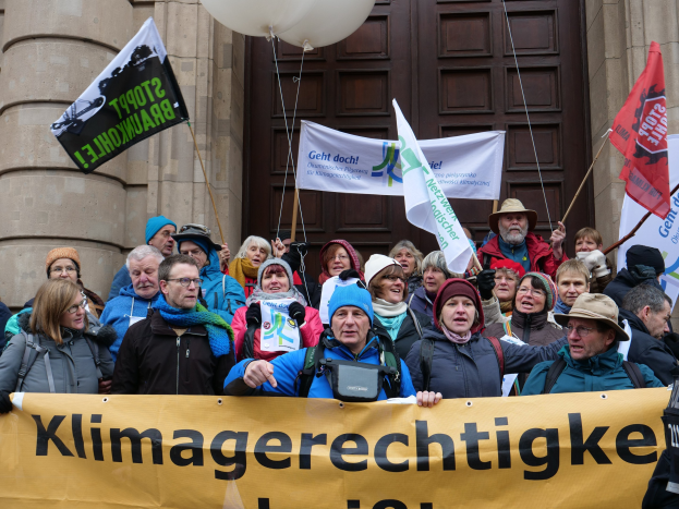 Gruppe von Menschen mit Spruchbändern, Fahnen und Luftballons vor einem Gebäude mit Säulen und einer Tür während eines Klimastreiks in Deutschland.