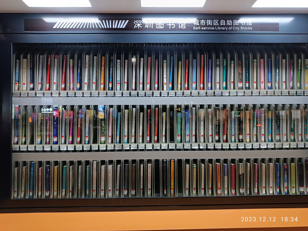 Eine gut beleuchtete Bibliothek mit hohen Bücherregalen voller Bücher, eine sichtbare Tafel mit Text und ein Wasserzeichen unten, das an eine Selbstbedienungsbibliothek in Stadtblocks erinnert.