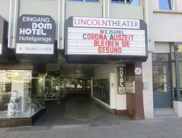 Das Lincoln Theater in Berlin, Deutschland, ein Gebäude mit Glasfenstern und -türen und einer Tafel mit Text darauf, mit verschiedenen Gegenständen im Inneren, die einen pulsierenden Stadtbild Eindruck vermitteln.