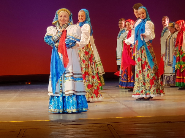 Eine Gruppe von Menschen in leuchtend bunten, detaillierten traditionellen ukrainischen Kostümen, die auf einer Bühne lächeln.