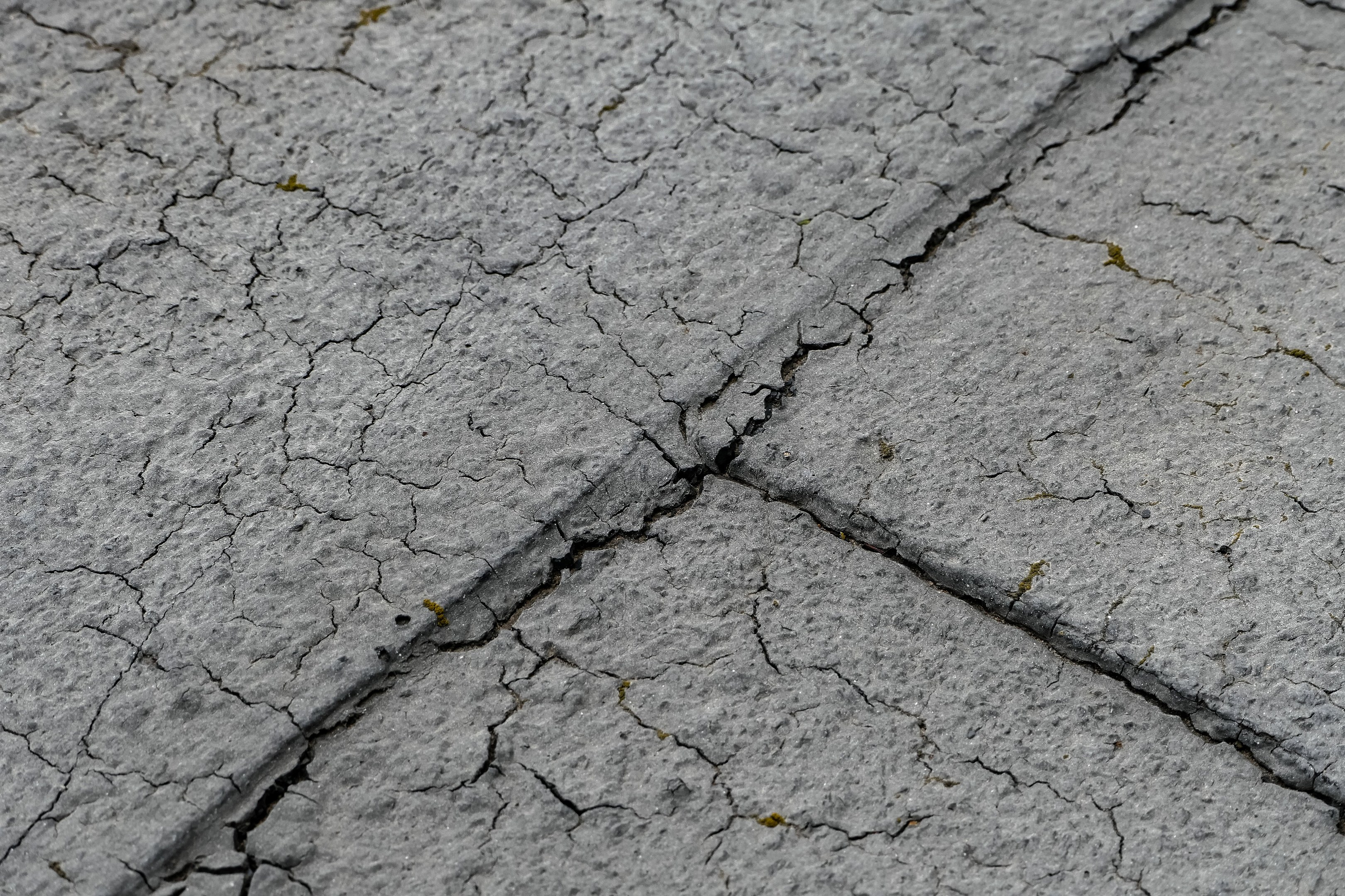 Nahaufnahme einer gebrochenen und verwitterten Straßenoberfläche mit tiefen, breiten Rissen.