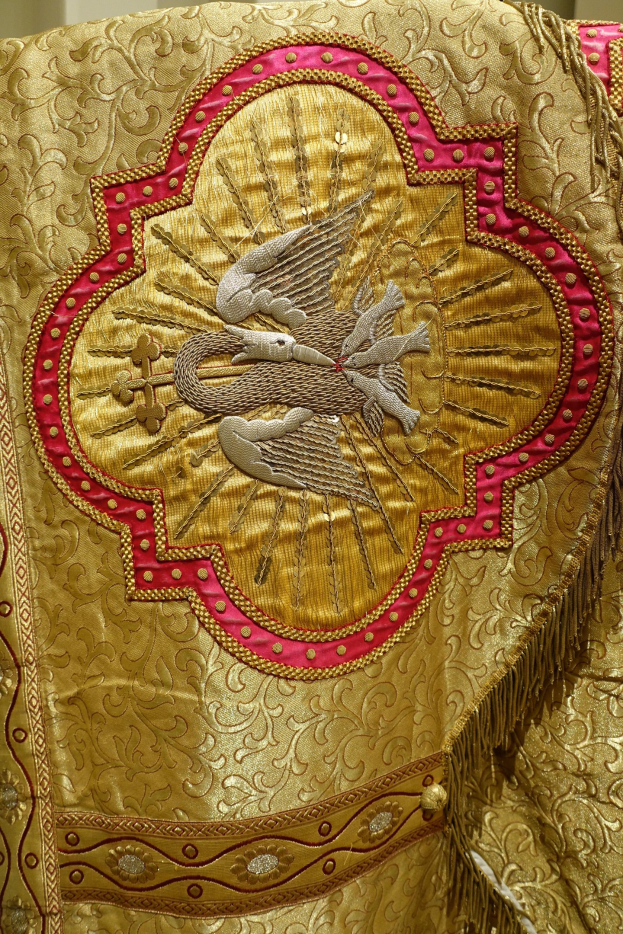 Nahaufnahme eines Priestergewandes mit aufwendiger Gold- und Roterstickerei und einem luxuriösen, königlichen Design an einer Wand im Hintergrund.