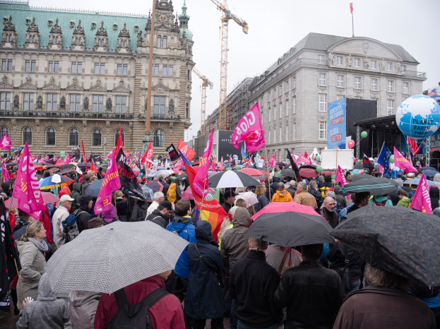 Eine große Gruppe von Menschen nimmt an einer Frauen-Demo in Berlin teil und steht vor einem Gebäude, während sie Schirme, Plakate und Luftballons halten.