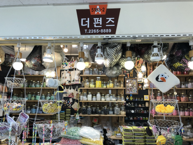 Ein unordentlicher Laden in Seoul, der verschiedene Gegenst%C3%A4nde wie K%C3%B6rbe, Lichter, Flaschen und Spielzeuge auf Regalen ausstellt, mit einer Tafel oben, die anzeigt, dass es einer der besten koreanischen L%C3%A4den ist.
