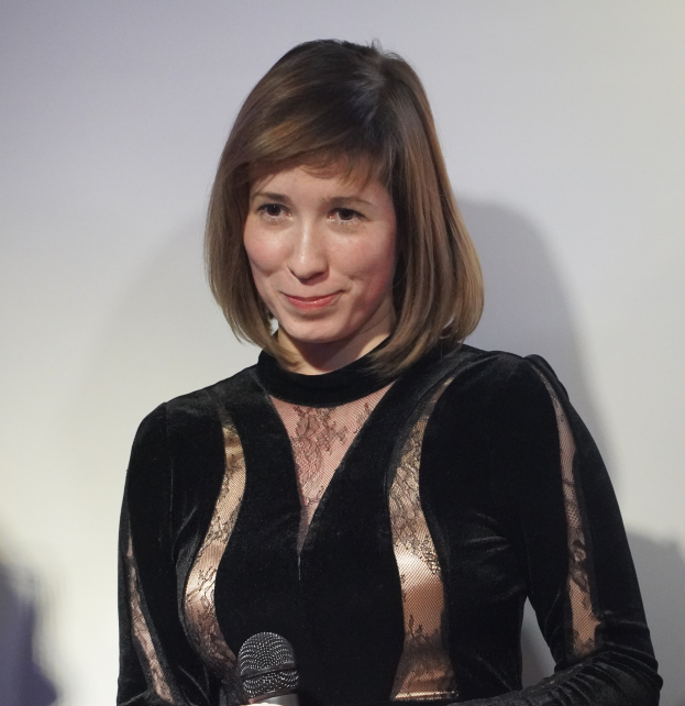 Eine Frau in einem schwarzen Kleid hält ein Mikrofon und steht vor einer Wand, mit einem selbstbewussten und entschlossenen Gesichtsausdruck während eines BBC Radio 1-Interviews.