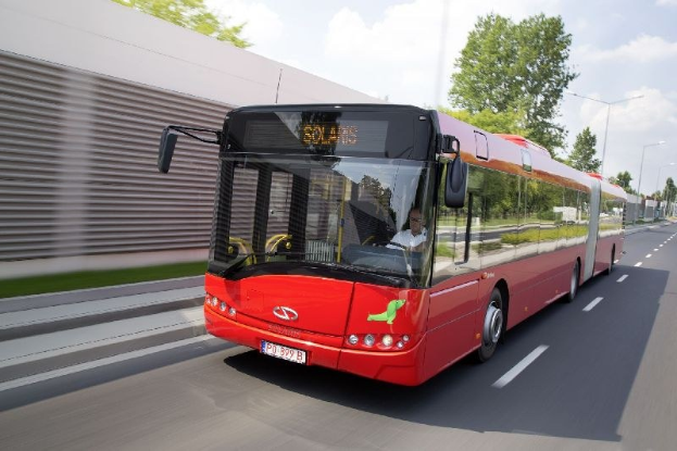 Ein roter Bus fährt auf einer Straße neben einem Gebäude, mit einer Person im Inneren.
