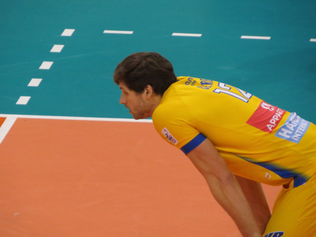 Eine professionelle Volleyballspielerin in einem gelben "Volleyball"-T-Shirt steht selbstbewusst auf einem Court und ist bereit, den Ball zu servieren.