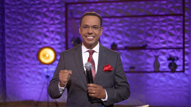 Stephen Colbert, Moderator von 'The Daily Show with Trevor Noah', steht auf einer Bühne und hält ein Mikrofon in der Hand, trägt einen Anzug, eine Krawatte und eine Brille.