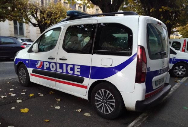 Ein Polizeiwagen steht an der Seite einer Straße mit Gebäuden, Bäumen und heruntergefallenen Blättern im Hintergrund.