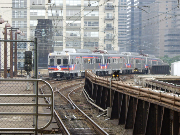 Ein Nahverkehrszug fährt an hohen Gebäuden entlang der Bahnschienen vorbei.
