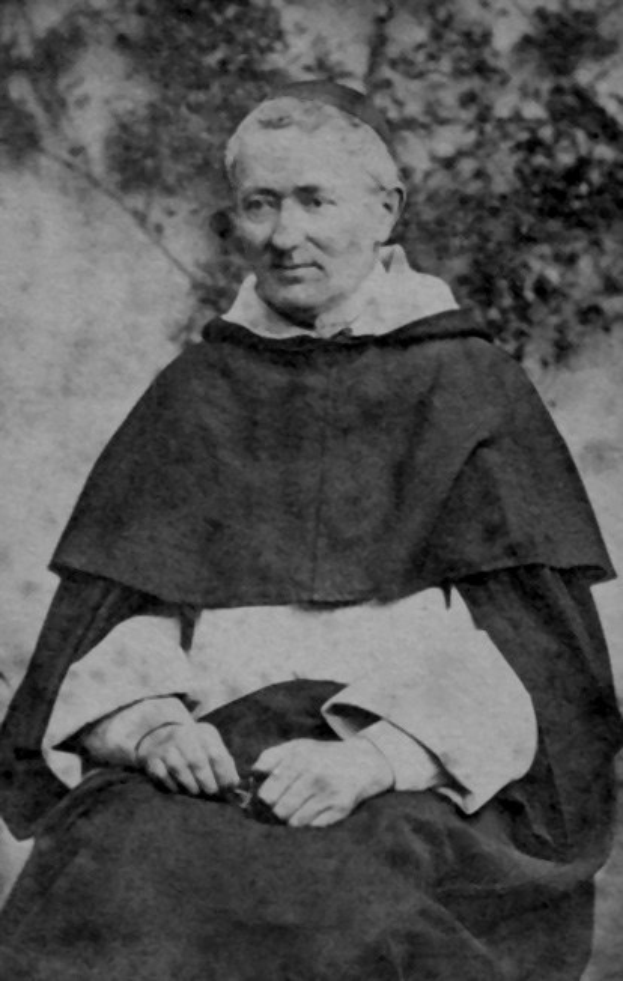 Ein Schwarz-Weiß-Foto eines alten Mannes in Priesterroben, der mit gefalteten Händen im Gebet sitzt, vor einem Baum Hintergrund beleuchtet.