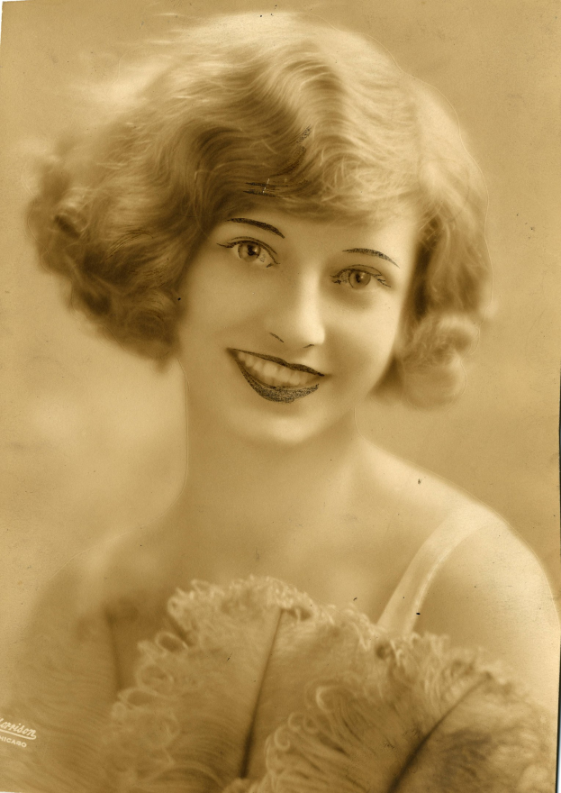 Ein Schwarz-Weiß-Foto einer Frau in einem Kleid im Stil der 1920er Jahre mit einer klassischen Bob-Frisur, die warm lächelt.