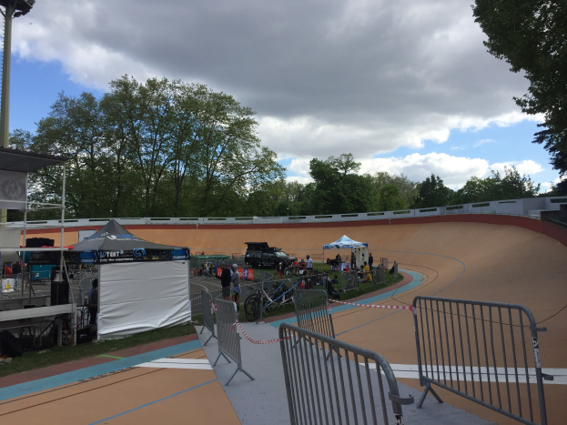 Gruppe von Radfahrern, die auf einer Schmutz-BMX-Strecke mit Geländern, Zelten und Fahrzeugen im Hintergrund, Bäumen und einem bewölkten Himmel während der 2018 UCI BMX-Weltmeisterschaften fahren.