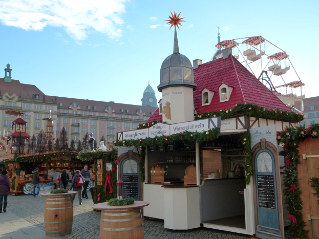 Ein geschäftiger Weihnachtsmarkt in Nürnberg, Deutschland mit Menschen um dekorierte Stände, festliche Lichter, ein Riesenrad, Gebäude und ein Schild an der rechten Seite.