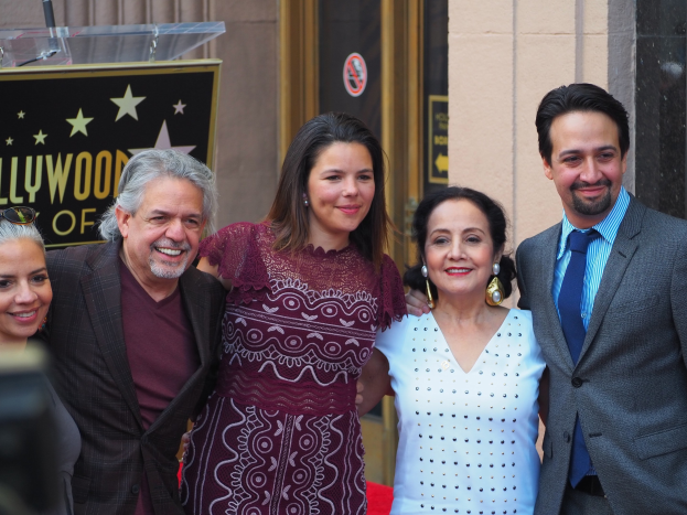Gruppe von Menschen auf einem roten Teppich bei der Zeremonie des Hollywood Walk of Fame, mit einer Tafel, einem Glaspodest und einer Wand im Hintergrund.