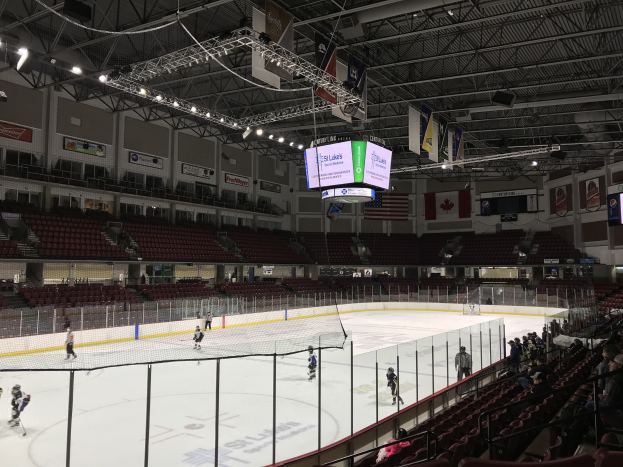 Ein Hockey-Spiel in einer großen Arena mit einem zentralen Netz, Zuschauern auf beiden Seiten, Deckenleuchten und Trägern sowie Bannern an den Wänden, die als St. Louis Blues Arena gekennzeichnet sind.
