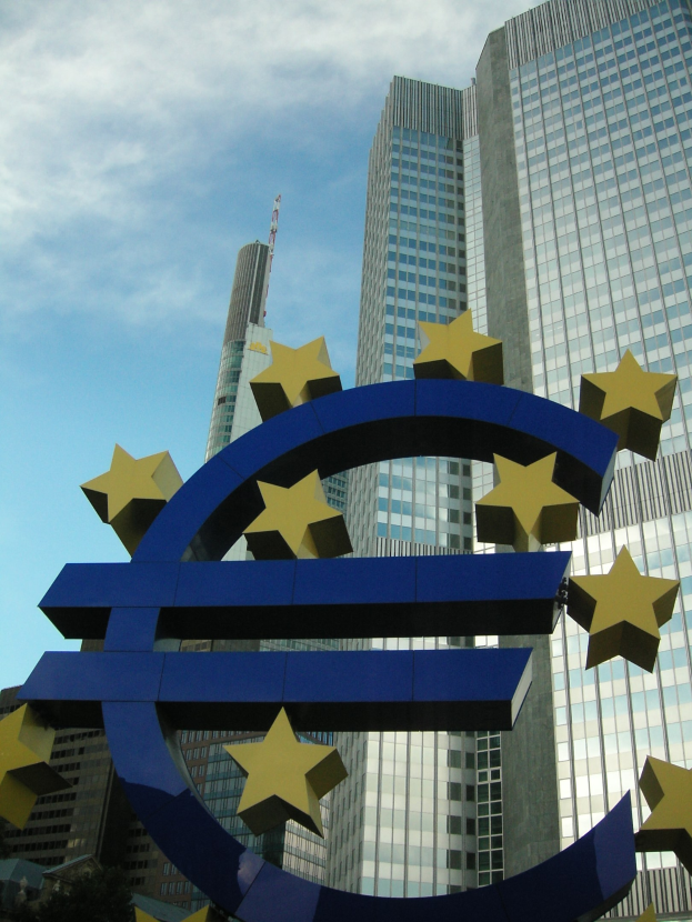 Eurozeichen vor dem Europäischen Zentralbank-Hauptquartier in Frankfurt, Deutschland, mit Bäumen und einem bewölkten Himmel.