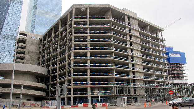 Ein großes Bauprojekt in einer städtischen Umgebung, umgeben von Wolkenkratzern, mit Fahrzeugen, Fußgängern, Verkehrsinfrastruktur und Kränen unter einem klaren Himmel.