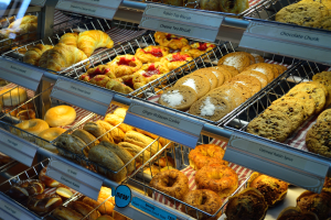 Ein Bäckereischaufenster voller verschiedener Teilchen, Kuchen, Kekse und andere Backwaren, mit Schildern, die die Art der Backwaren angeben.