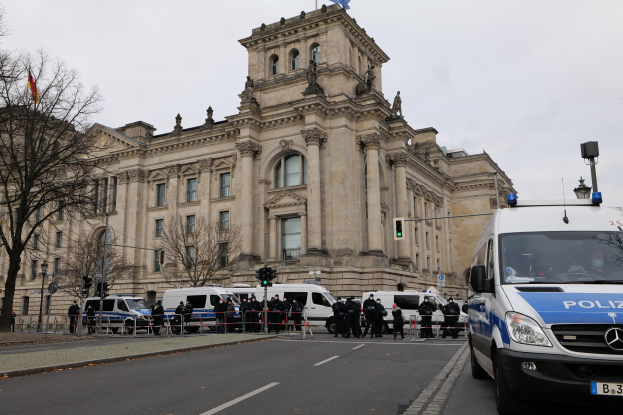 Polizisten vor dem Reichstaggebäude in Berlin, Deutschland, mit Fahrzeugen, einem Zaun, Verkehrszeichen, Laternen, Bäumen und Flaggen.