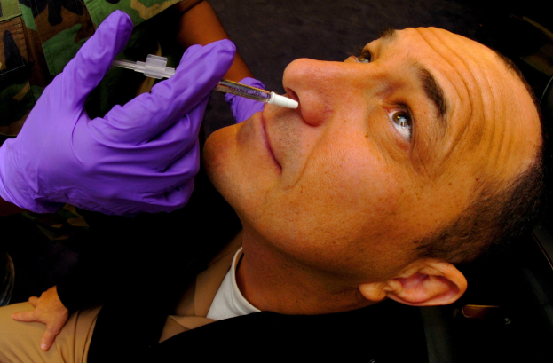 Ein Arzt in violetten Handschuhen spritzt einem Mann ein Vakzin mit einer Spritze in den Mund.