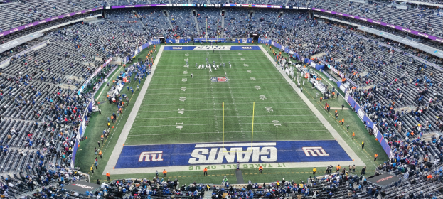 Ein überfülltes Fußballstadion mit Zuschauern, Spielern auf dem Feld, Torpfosten und Texttafeln, aus einer erhöhten Perspektive betrachtet.