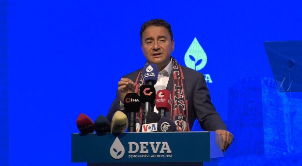 Mann in Mantel und Schal steht an Podium mit Mikrofonen, spricht zu einem Publikum mit einem Bildschirm und einem Objekt im Hintergrund; das Podium zeigt eine Tafel mit der Aufschrift "deva-Geschäftsführer sagt, es sei keine gute Idee für die Zukunft."